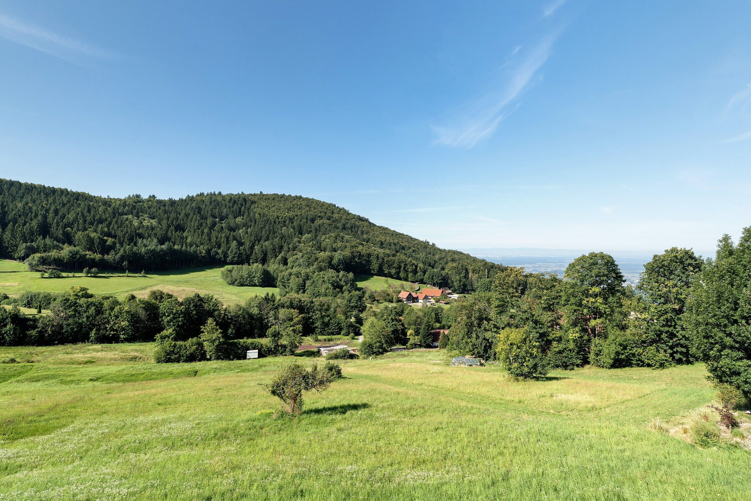 Un paysage rural caractérisé par des collines douces, un petit village et un ciel bleu dégagé.