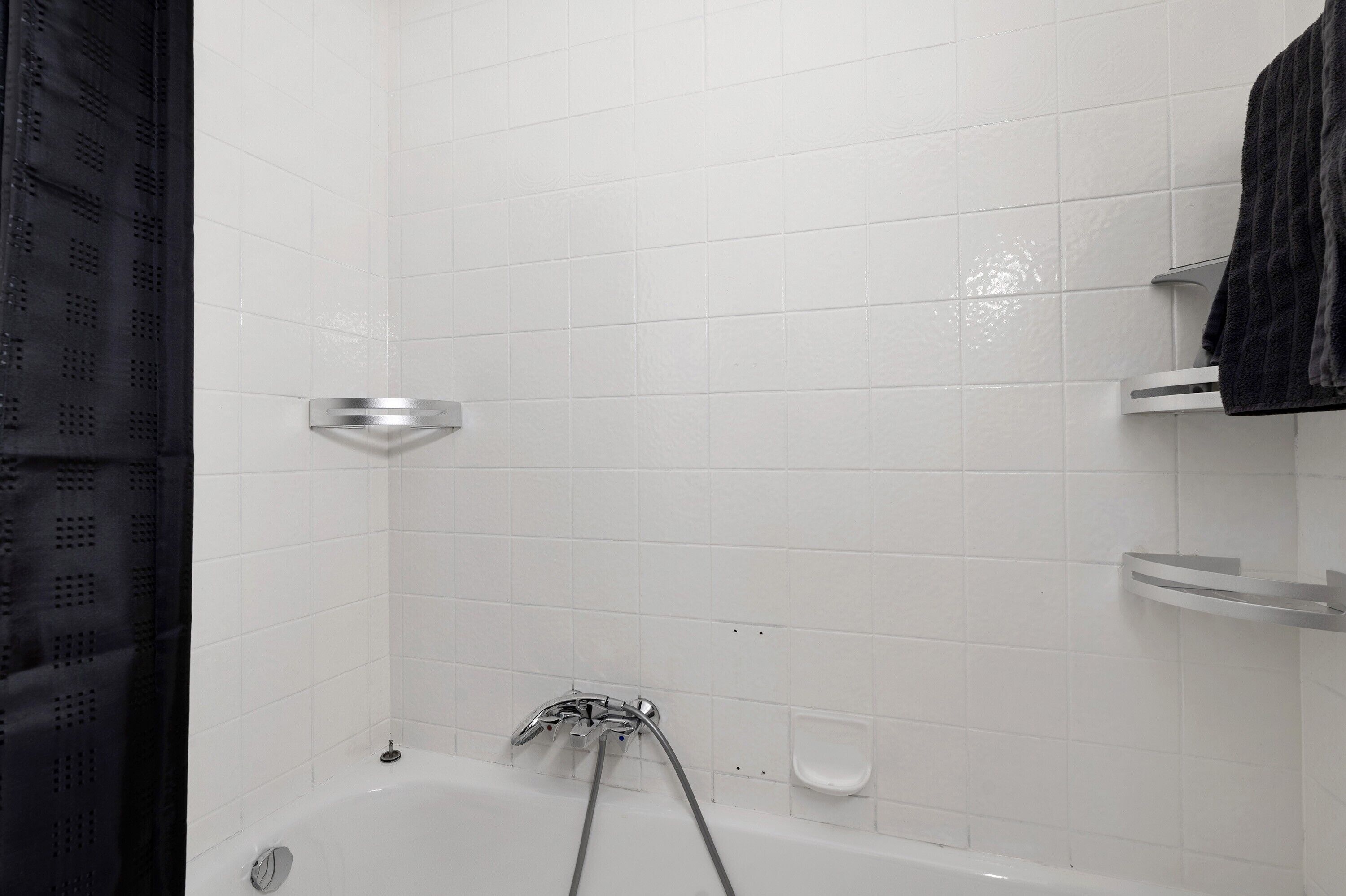 Een badkamer met witte betegelde wanden, een badkuip, een douchekop en een zeepbakje.