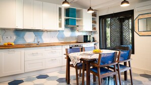 A modern kitchen with white cabinets, a blue backsplash, and a dining area with blue chairs and a table. - Caletta Nest 88 by Klodge – Sea view & pool (Porto Rotondo)