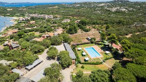 An aerial view of a coastal resort with multiple buildings, a swimming pool, and surrounding greenery. - Caletta Nest 88 by Klodge – Sea view & pool (Porto Rotondo)