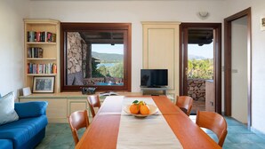 Un comedor con una mesa, sillas, una estantería, un televisor y vistas al exterior.