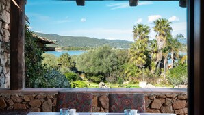 Una mesa dispuesta con un croissant, un plato y vasos, con vistas a un paisaje pintoresco de un lago y palmeras.