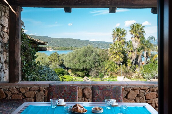 A table set with a croissant, a plate, and glasses, overlooking a scenic view of a lake and palm trees.