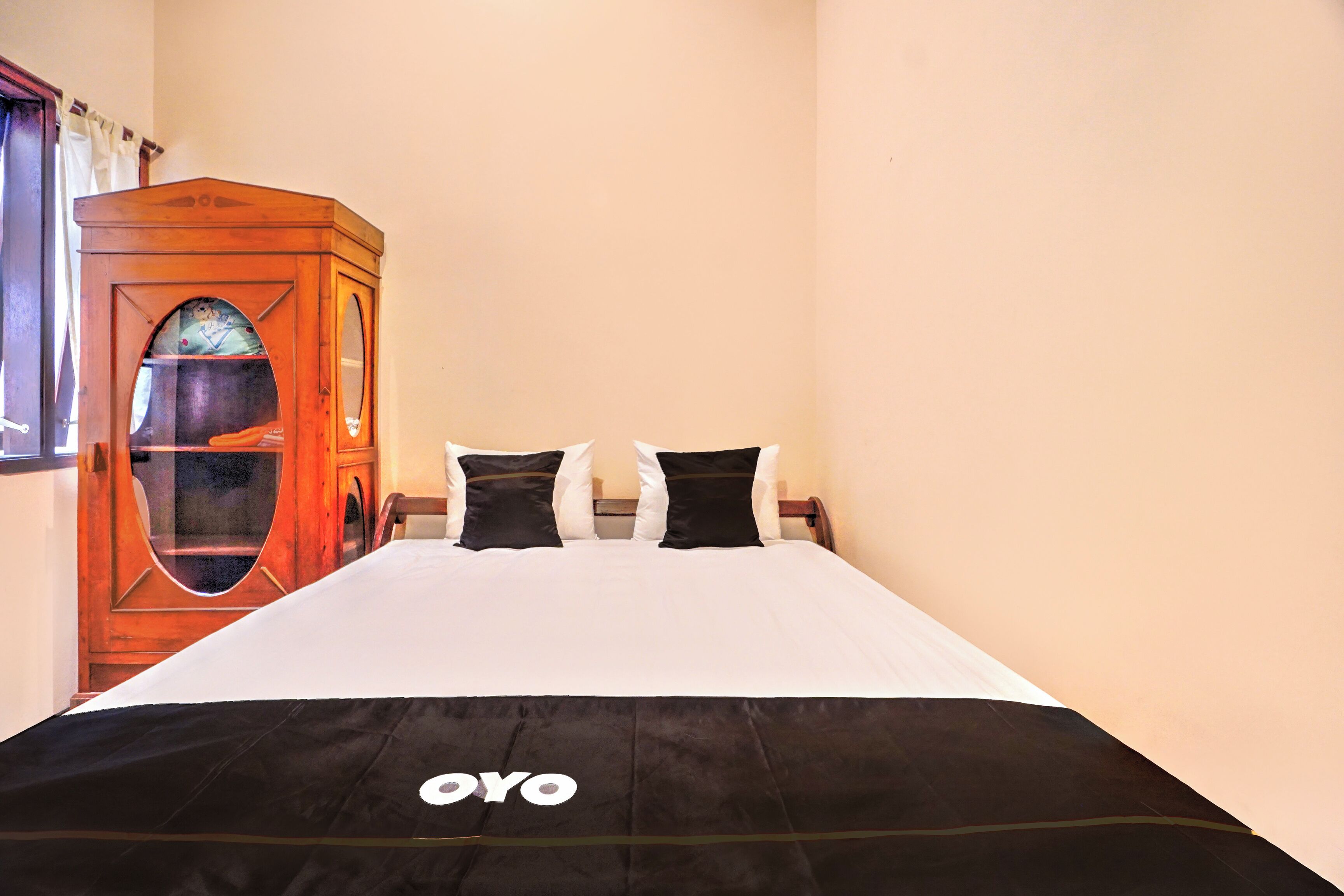 A hotel room with a bed, a wooden cabinet, and a window with curtains.