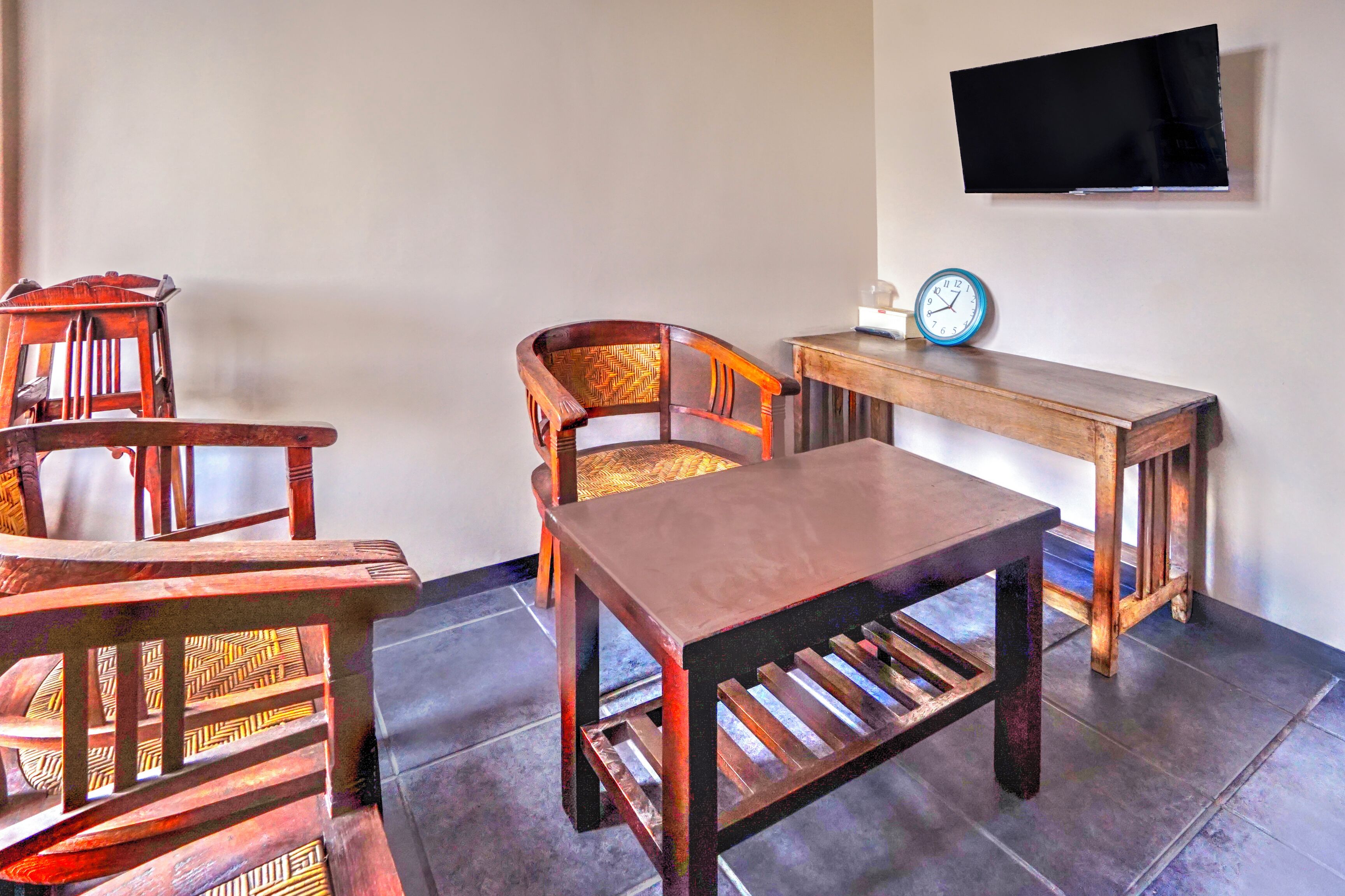 A room with a wooden table and two chairs, a television mounted on the wall, and a clock on the table.