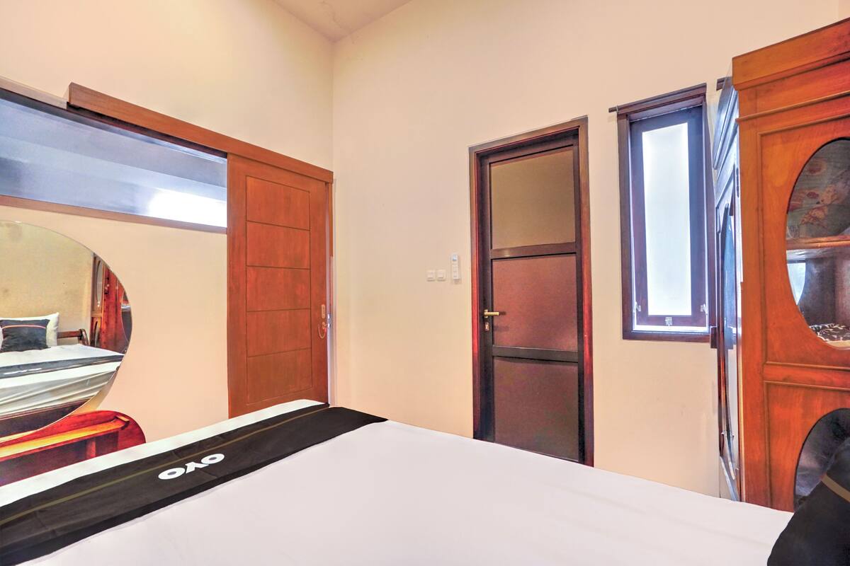 Habitació d'hotel amb un llit, una porta de fusta, una finestra i un mirall que reflecteix part de l'espai.