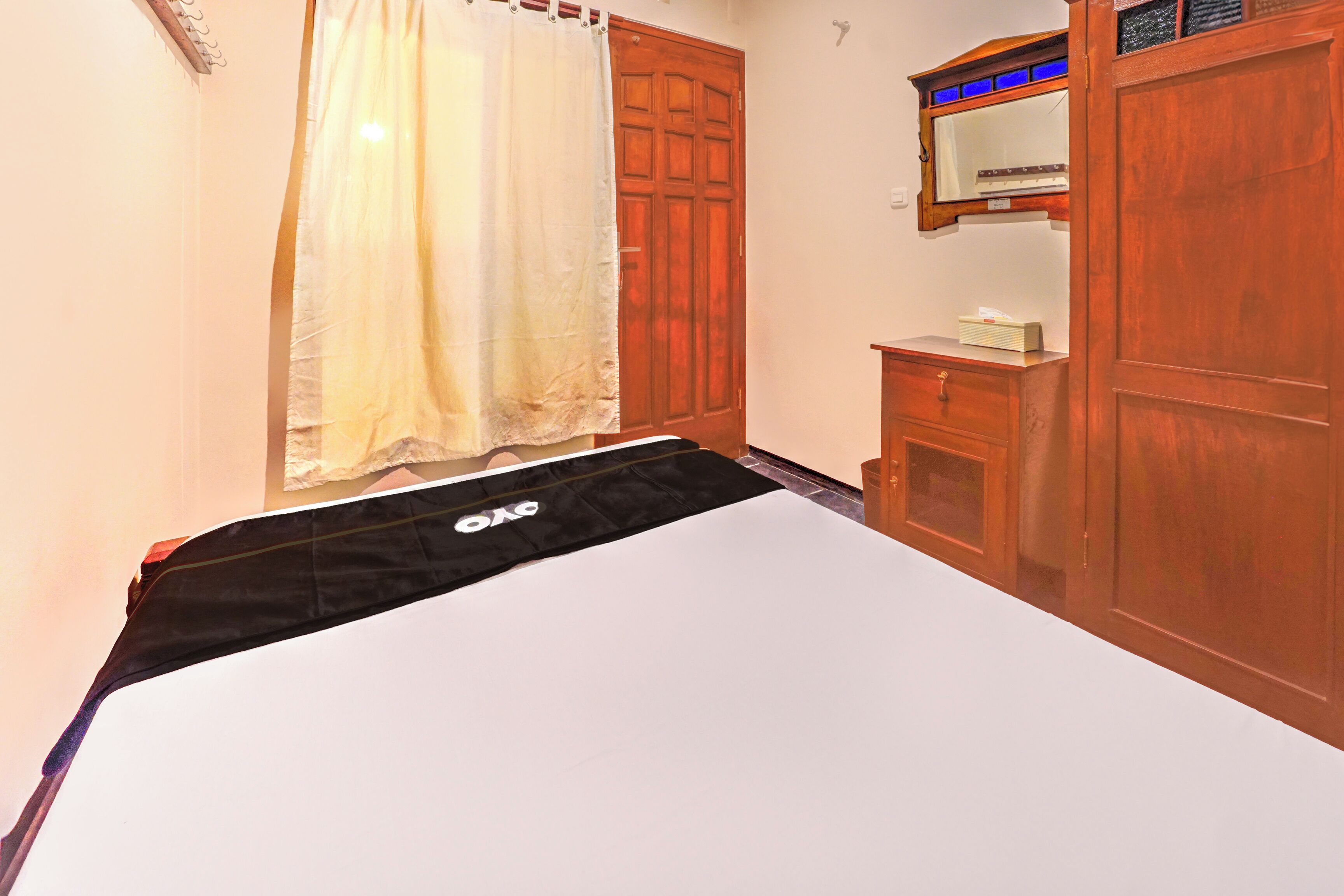 A bedroom with a bed, a wooden wardrobe, a small table, and a mirror.