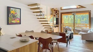Un intérieur moderne avec une table à manger en bois, des chaises, un escalier et une grande fenêtre donnant sur des arbres.