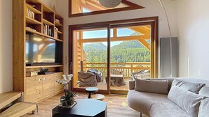 Un salon moderne doté d’un grand téléviseur, de meubles en bois, d’un canapé et d’un balcon offrant une vue sur les montagnes.