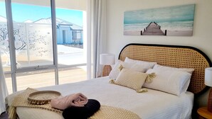 A bed with a woven headboard, white bedding, and a view of a beach through large windows. - Ace on Par - Central Dunsborough (Dunsborough)