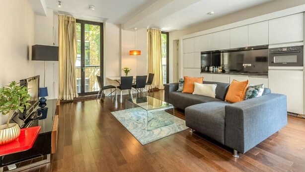A modern living room with a grey sofa, a glass coffee table, and a dining area with chairs and a table.