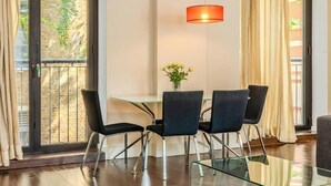 A modern dining area with a glass table, four chairs, and a hanging orange pendant light.
