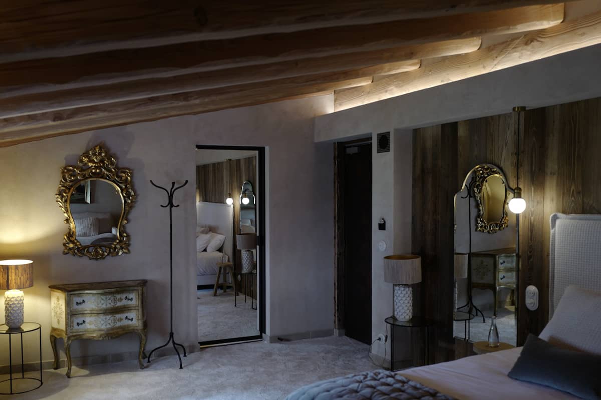 A bedroom with a large bed, a wooden ceiling, a mirror, and a dresser.