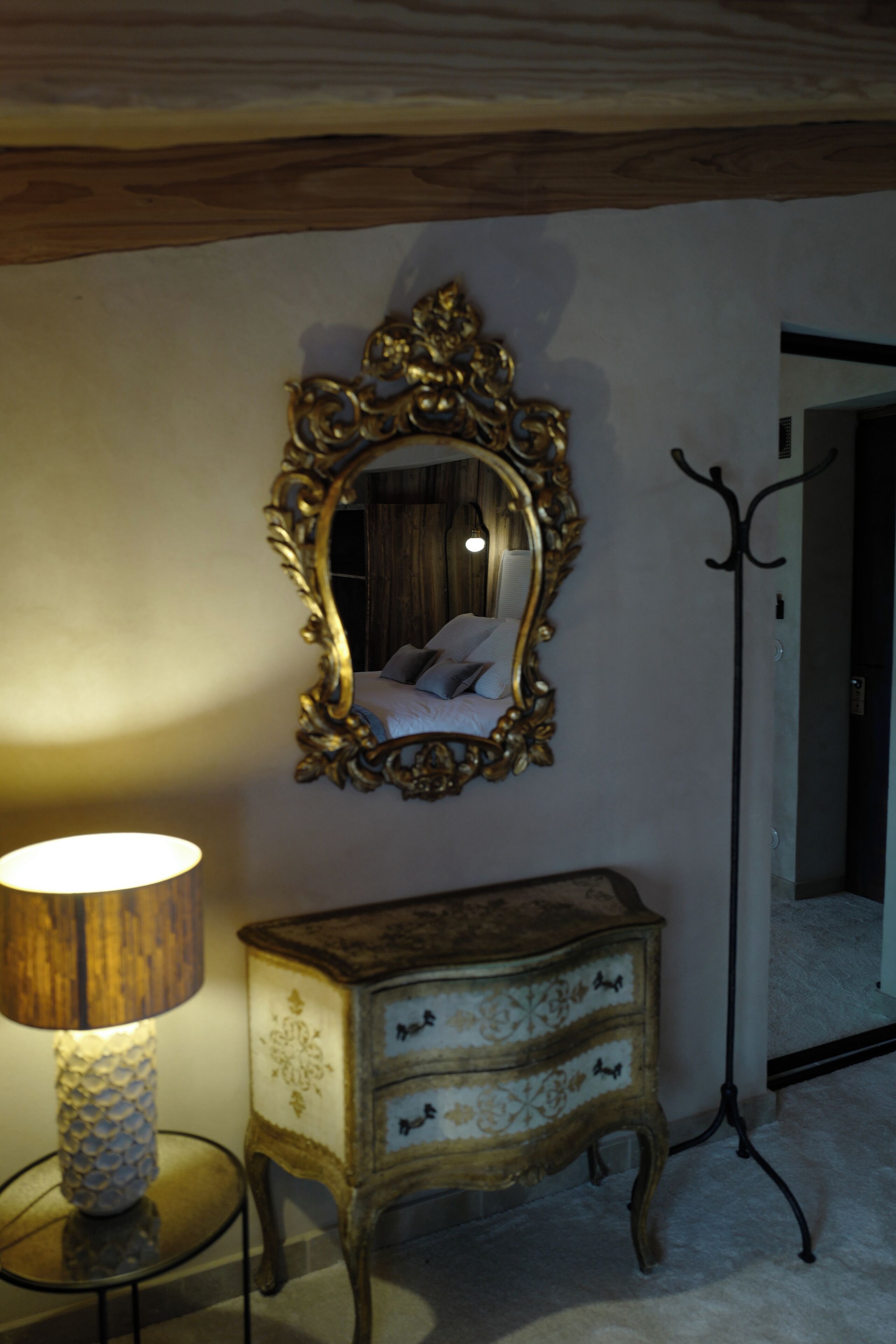 A bedroom with a large ornate mirror, a bedside lamp, and a vintage dresser.
