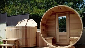 Eine Saunakabine aus Holz mit einer Bank und einem kleinen Tisch, umgeben von einer Holzterrasse.
