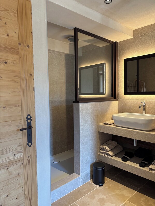 Un baño moderno con puerta de madera, cabina de ducha de vidrio, lavabo con espejo y toallas ordenadas.