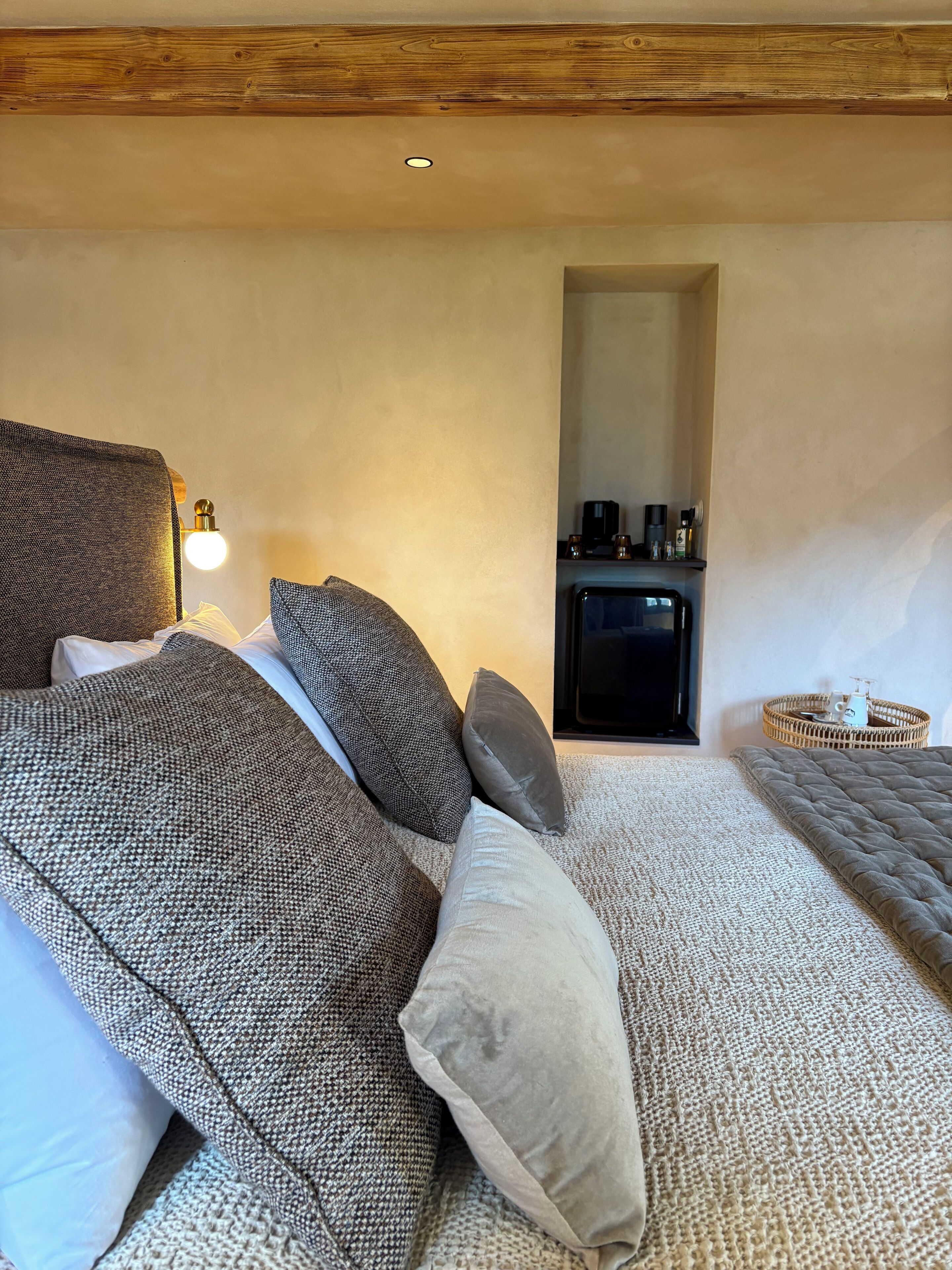 A bedroom with a bed, pillows, a bedside table with a lamp, a small cabinet, and a wicker basket.