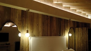 Ein gemütliches Schlafzimmer mit Holzboden, einem großen Bett mit vielen Kissen und einem kleinen Hocker.