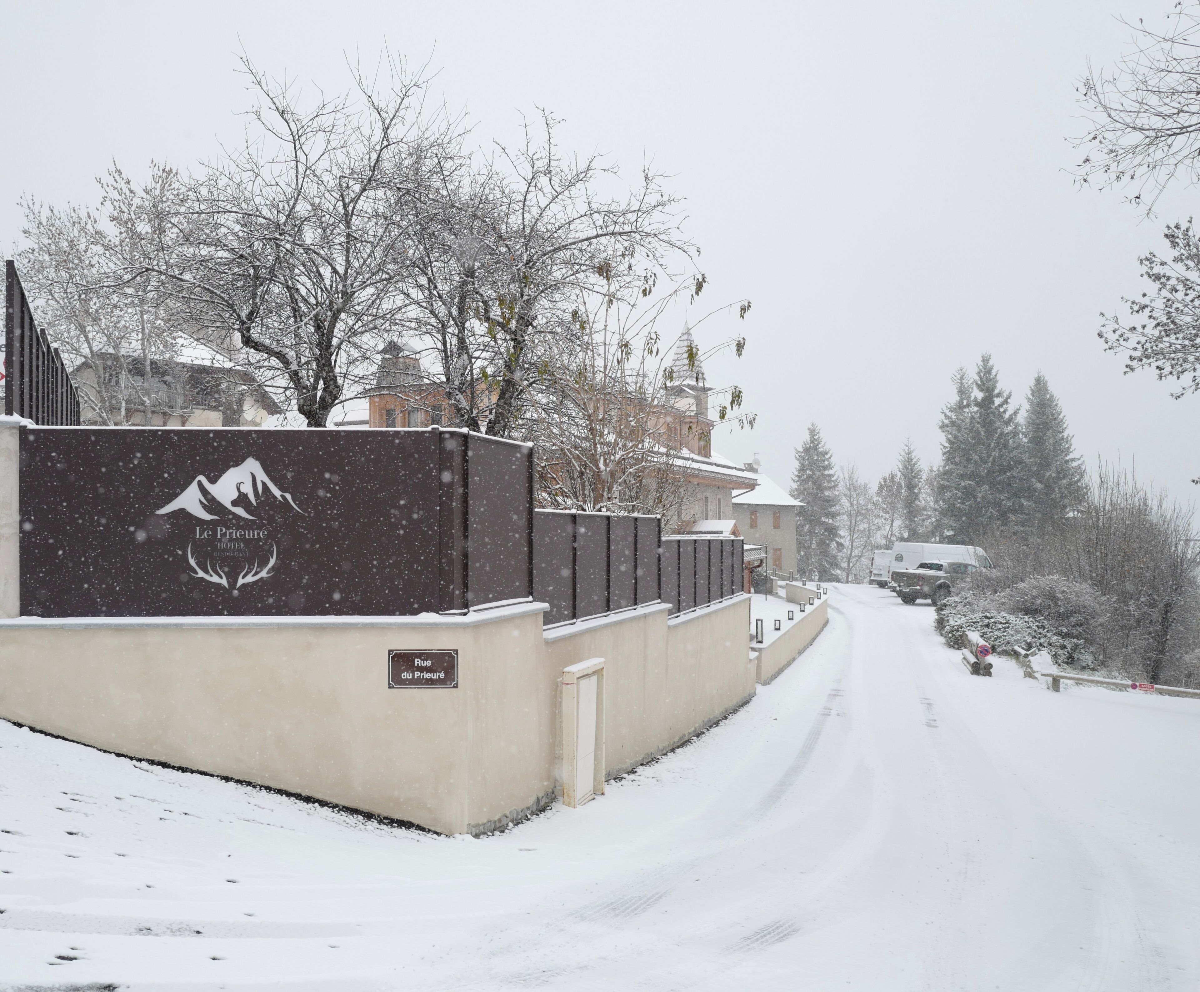 Eine verschneite Straße führt zu einem Hotel mit Berglogo an der Wand.