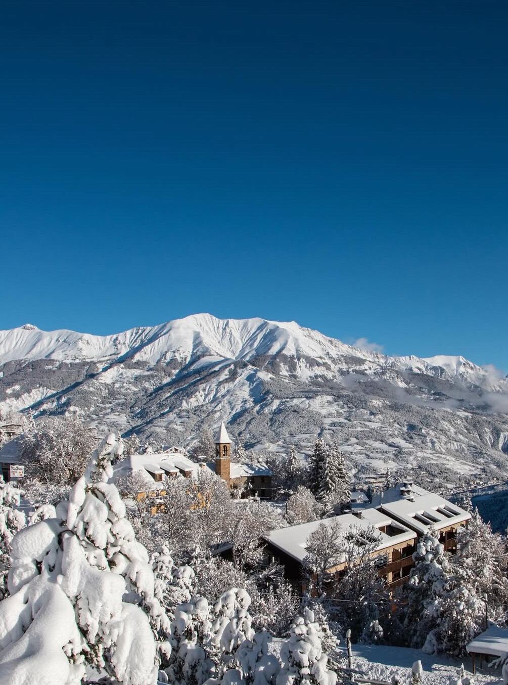 Un paysage montagneux enneigé, avec une église et des bâtiments au premier plan.