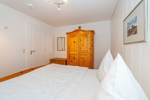 A bedroom with a bed, a wooden wardrobe, a bedside table, and a framed picture on the wall.