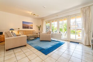 Ein geräumiges Wohnzimmer mit einem großen Fenster, einem blauen Teppich und einem Gemälde an der Wand.
