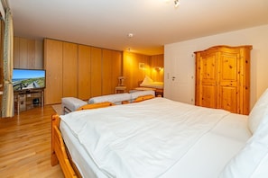 A bedroom with a large bed, wooden wardrobe, and a television on a wooden cabinet.