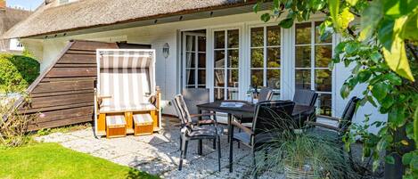 A house with a covered patio, a dining table with chairs, and a large window overlooking the garden.