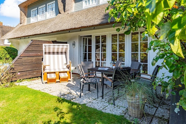 A house with a covered patio, a dining table with chairs, and a large window overlooking the garden.