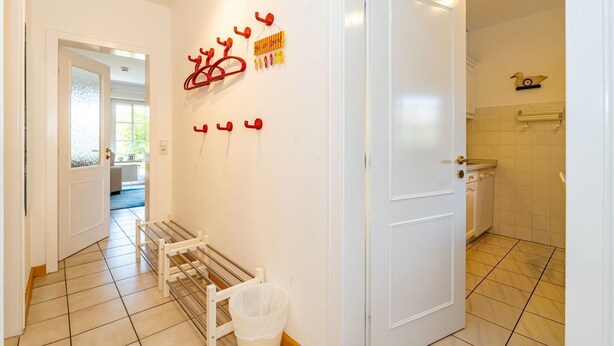 A hallway with a white door, a drying rack, and a trash bin. - Rüm hart - Spacious vacation apartment Rüm hart on Sylt with terrace for max. 5 persons. (Sylt-Ost)