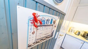 Une cuisine avec des meubles blancs, un décor représentant un homard rouge et un pare-feu en carreaux bleus et blancs.