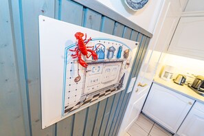 Una cocina con un armario blanco, una decoración de langosta roja y un salpicadero de azulejos azules y blancos.