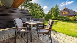 An outdoor patio with a table and four chairs, a bottle of wine, and a menu on the table. - Rüm hart - Spacious vacation apartment Rüm hart on Sylt with terrace for max. 5 persons. (Sylt-Ost)