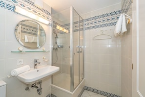 A bathroom with a glass-enclosed shower, a sink with a mirror above it, and patterned tiles on the walls.
