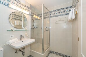 A bathroom with a glass-enclosed shower, a sink with a mirror above it, and patterned tiles on the walls.