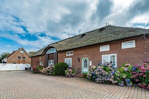 A brick building with a thatched roof, a gated driveway, and a variety of hydrangea bushes in front.