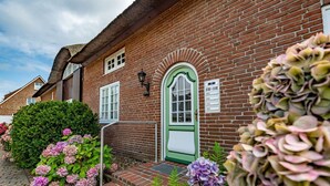 A brick building with a green door, white windows, and a small porch. - Goofys Will - Modern vacation apartment Goofys Will on Sylt with comfort and (Sylt)