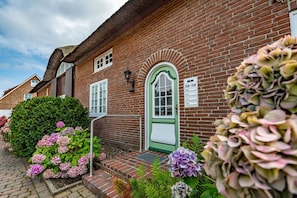 Un bâtiment en briques avec une porte verte, des fenêtres blanches et un petit porche.