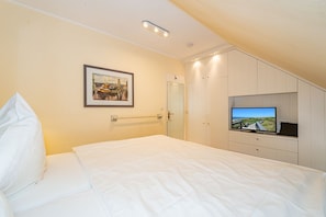 A hotel room with a bed, a television, a wardrobe, and a framed picture on the wall. - Goofys Will - Modern vacation apartment Goofys Will on Sylt with comfort and (Sylt)