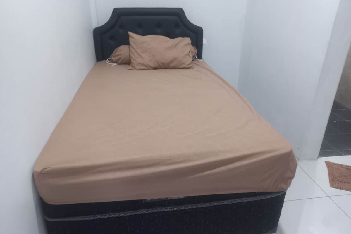 A small, single-bed room with a black headboard and a beige mattress cover.