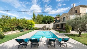 Une piscine rectangulaire, bordée d’une terrasse carrelée, entourée d’un jardin bien entretenu et d’un mur en pierre.
