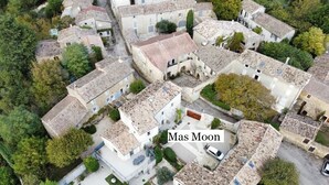 Vue aérienne d’un quartier résidentiel caractérisé par une architecture traditionnelle, avec des bâtiments en pierre surmontés de toits en tuiles et une piscine.