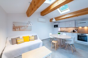 A modern apartment with a loft-style ceiling, a dining area, a kitchen, and a living room with a sofa and decorative pillows. - Closed as of today (Colonzelle)