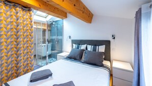 Une chambre à coucher comprenant un lit, des tables de chevet, une commode, un espace douche et une porte en verre donnant sur une salle de bain.