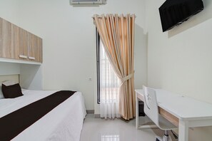 A hotel room with a bed, a desk, a chair, a TV, and a window with curtains.