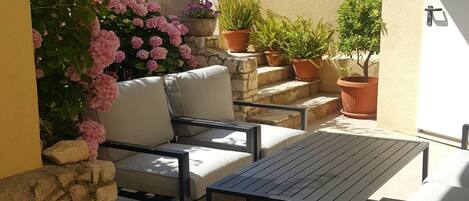 An outdoor seating area with a sofa and table, surrounded by potted plants and flowers.