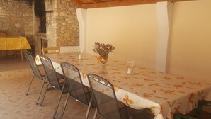 An outdoor dining area with a stone wall, a wooden ceiling, and a table with chairs.