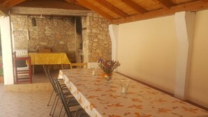 An outdoor dining area with a stone wall backdrop, a table with a floral tablecloth, and a vase with flowers.