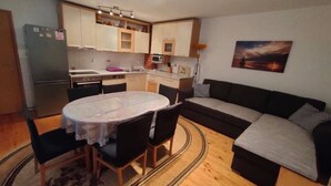 A compact living space with a dining table, chairs, a sofa, a kitchen area, and a painting on the wall.
