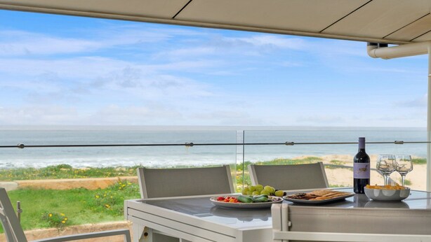 A balcony with a table set for a meal, overlooking a beach and ocean. - Time and Tides - Beachfront, Stunning Ocean Views. (THE ENTRANCE NORTH)